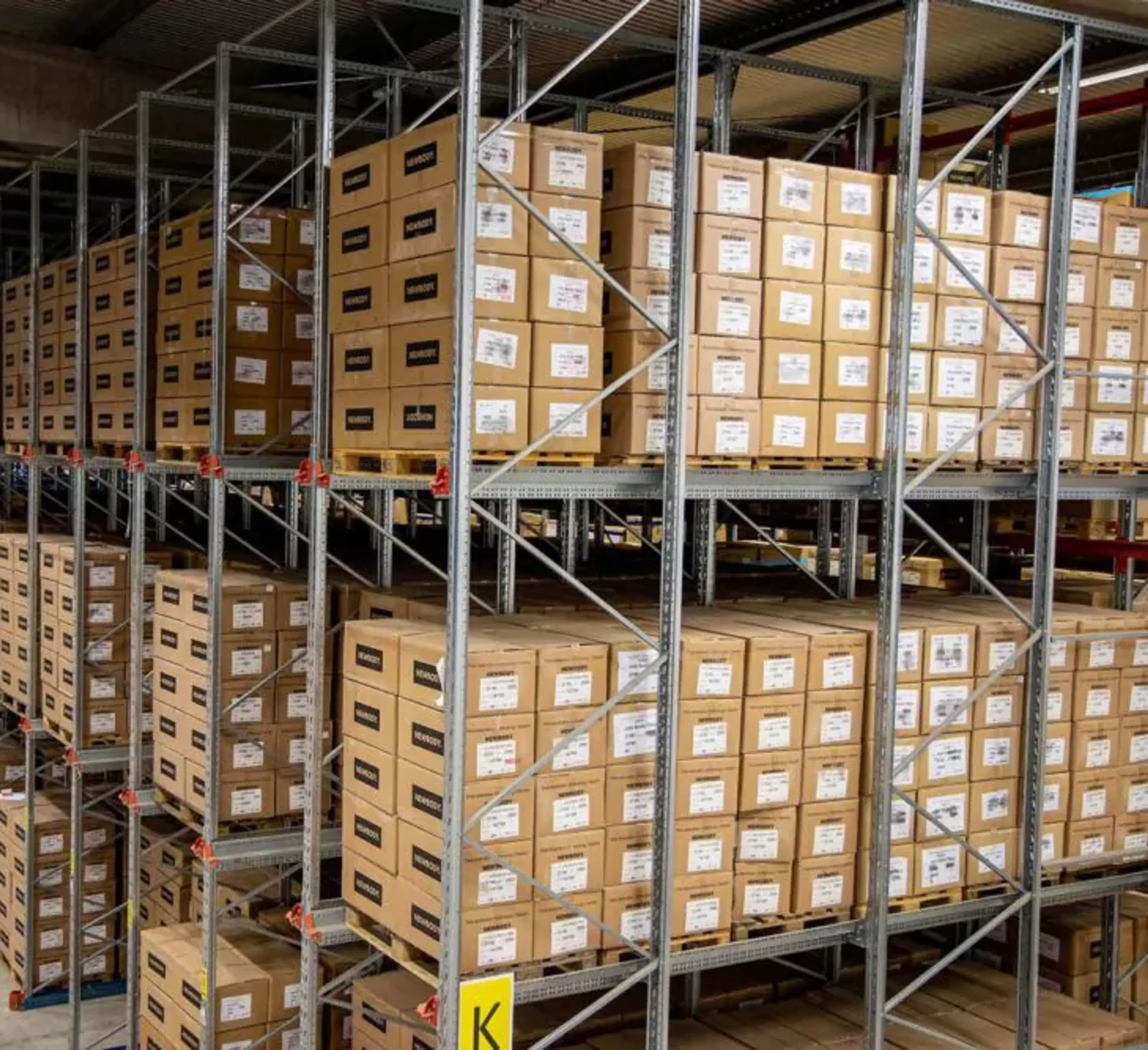 Hyllor fyllda med prydligt staplade kartonger i ett stort lagerutrymme. En översikt av välorganiserad förvaring i en ljus och rymlig lokal.