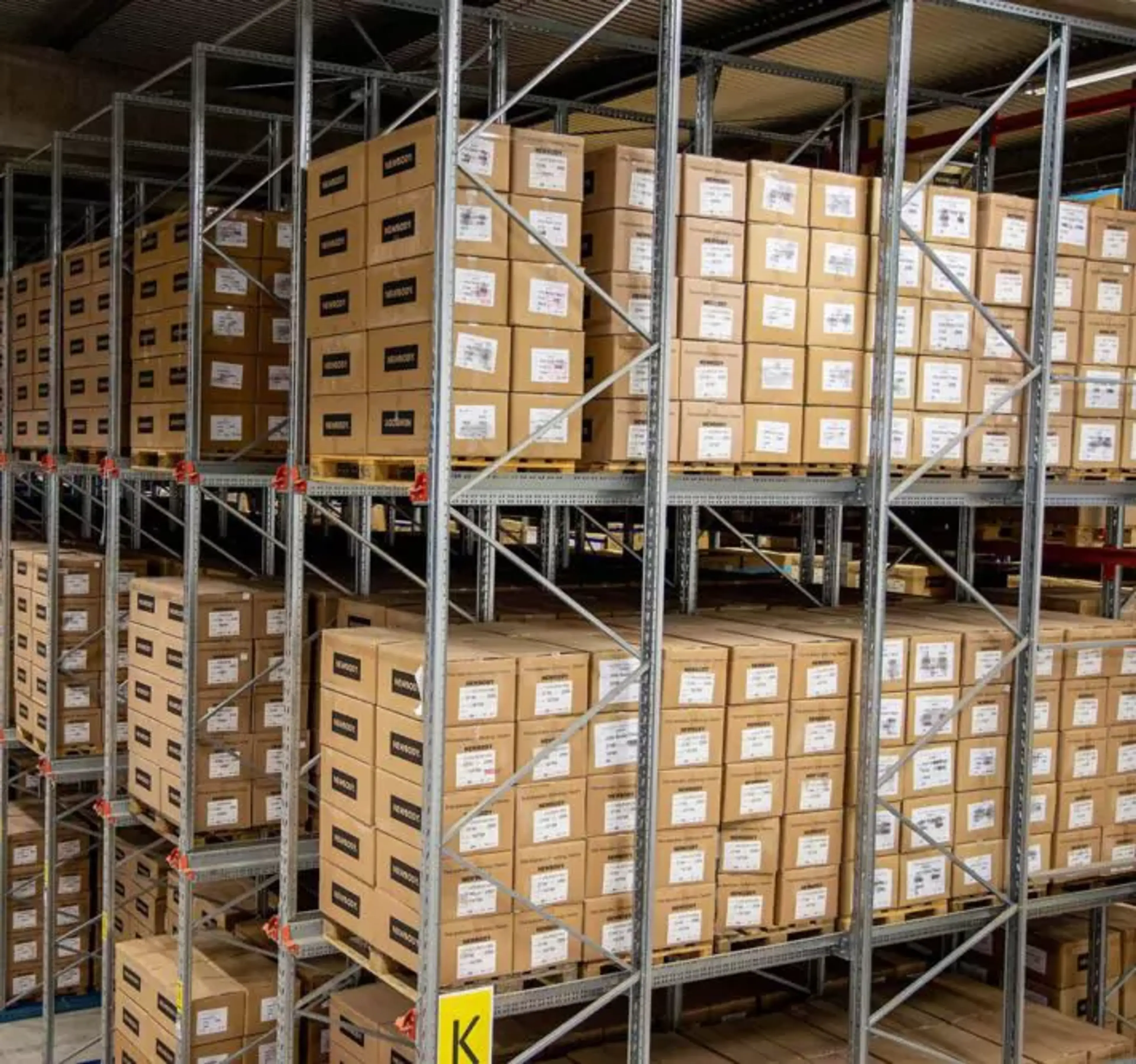 Hyllor fyllda med prydligt staplade kartonger i ett stort lagerutrymme. En översikt av välorganiserad förvaring i en ljus och rymlig lokal.