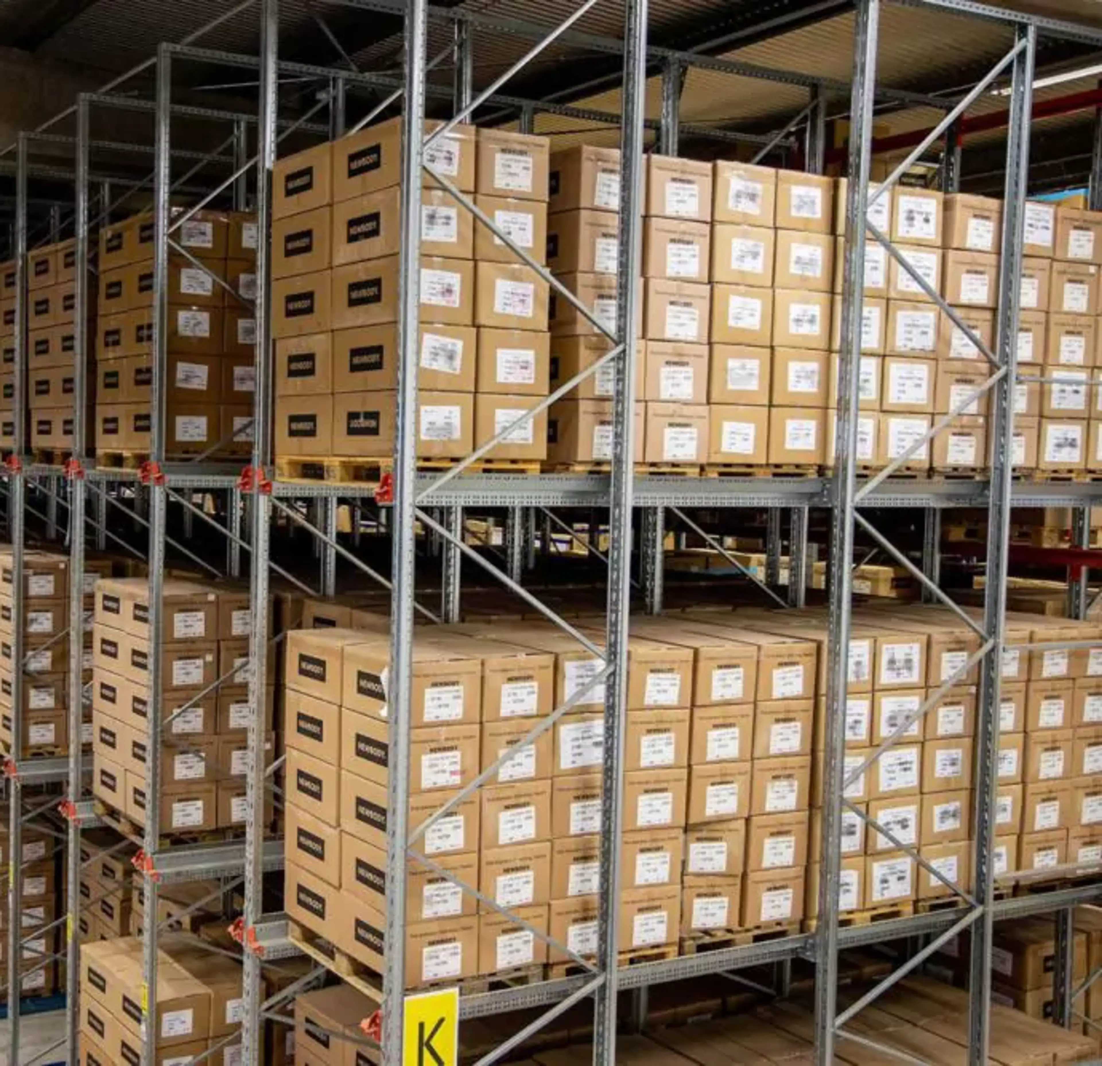 Hyllor fyllda med prydligt staplade kartonger i ett stort lagerutrymme. En översikt av välorganiserad förvaring i en ljus och rymlig lokal.
