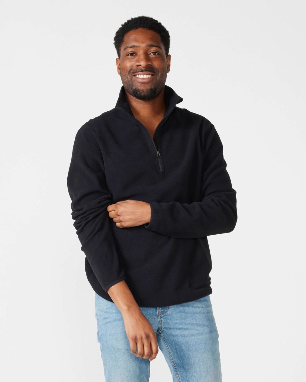 Mjuk svart fleece-tröja med halvlång dragkedja och upprätt krage, perfekt för kyliga dagar. Modellen bär tröjan med ärmarna lätt uppdragna och ett par ljusblå jeans.