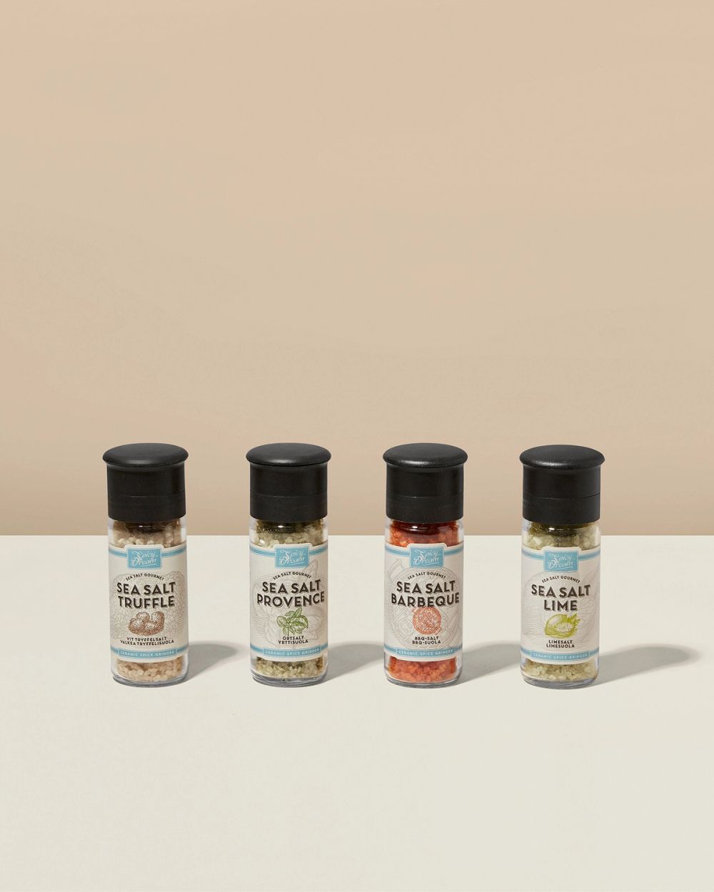 Fyra kryddburkar med keramiska kvarnar, innehållande olika smaksatta havssalter i beige och röda toner. Etiketterna visar smakerna tryffel, provence, barbeque och lime.