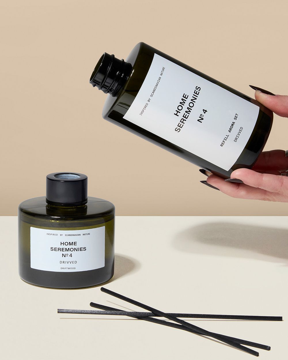 Ett doftset med en rund behållare och påfyllningsflaska i mörkgrönt glas, med svart text på vita etiketter. Svarta doftpinnar ligger bredvid behållaren.
