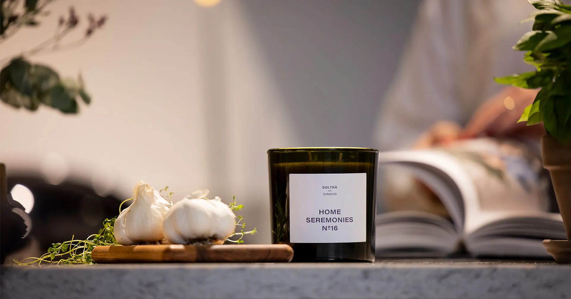 Doftljus står på en köksbänk med vitlök och basilika i bakgrunden