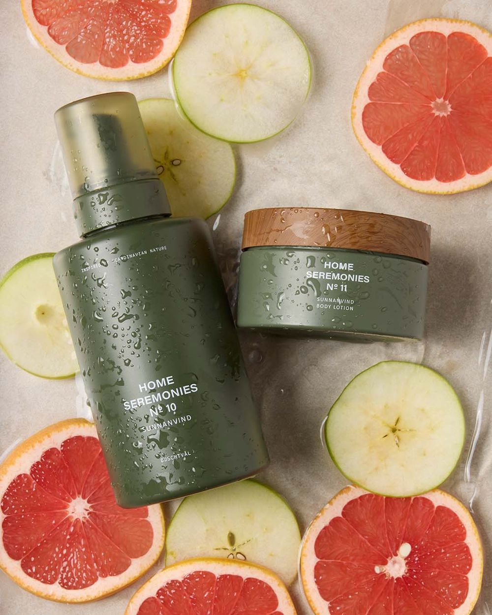 Set med dushtvål i skumform i pumpflaska och bodylotion i burk med trälock vackert arrangerade tillsammans med äpple och blodgrape