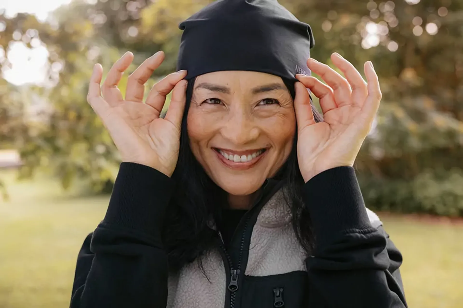 En varm mössa i mjukt material med en justerbar passform, här på en leende person utomhus. Mössan är svart och passande för kyligare dagar.