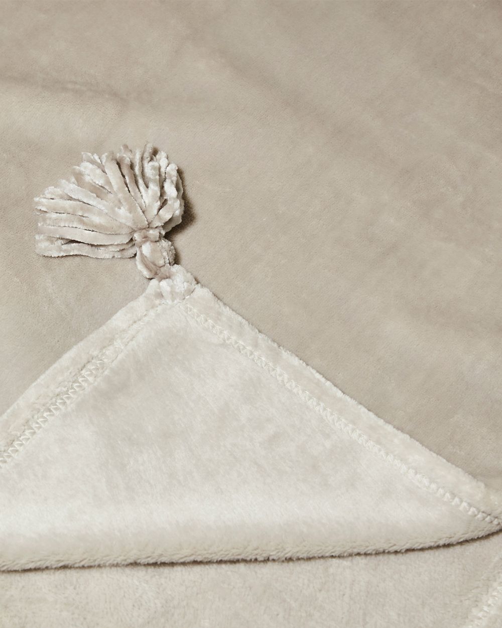 Mjuk, beige fleecefilt med dekorativ tofs i ena hörnet. Filten har en len och fin struktur som känns skön mot huden.