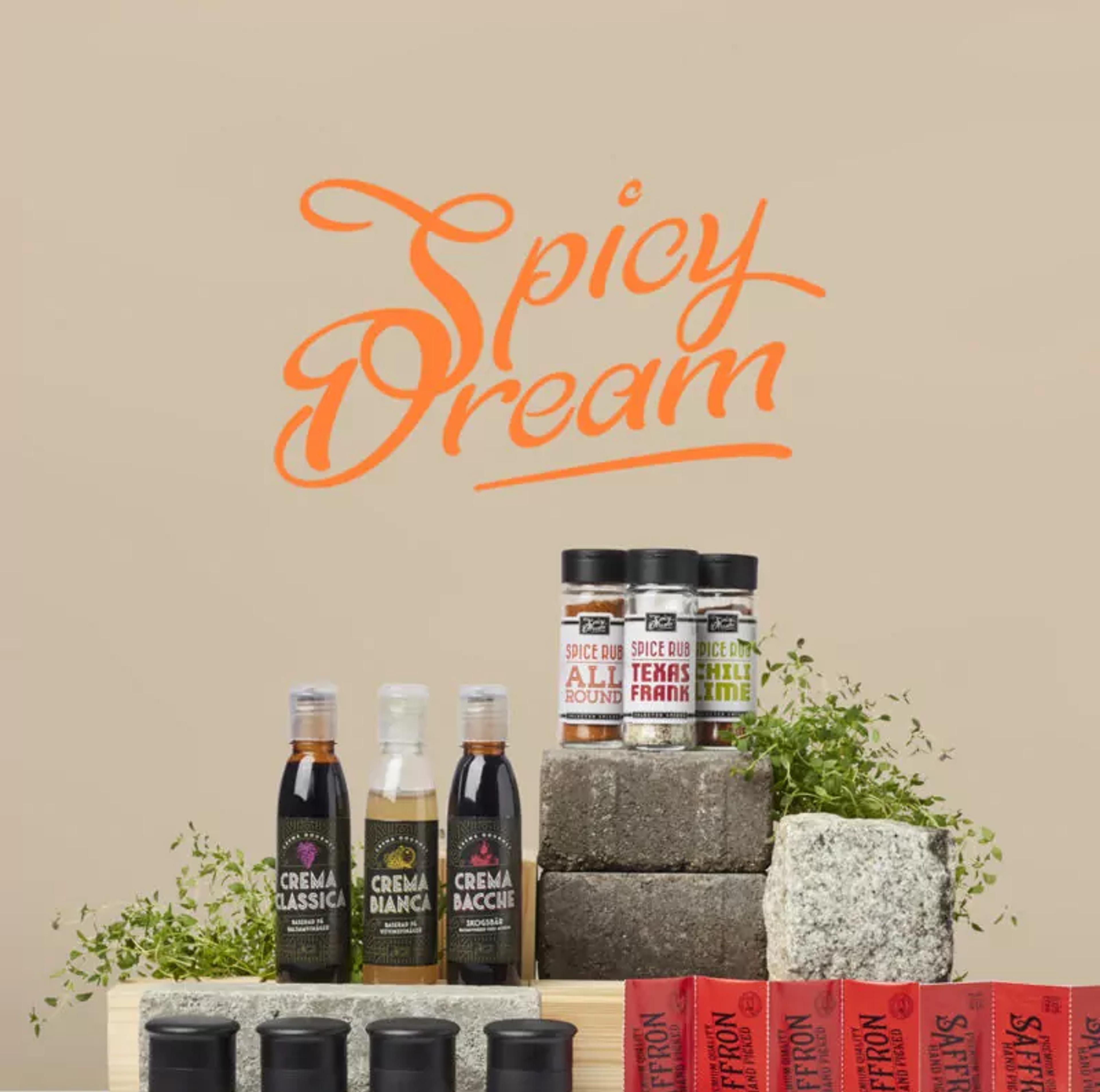 Ett urval av kryddor och såser i olika förpackningar, inklusive pepparmix, Himalaya-salt, svartpeppar, havssalt och saffran, arrangerade på tegelstenar och träblock. Ovanför lyser texten “Spicy