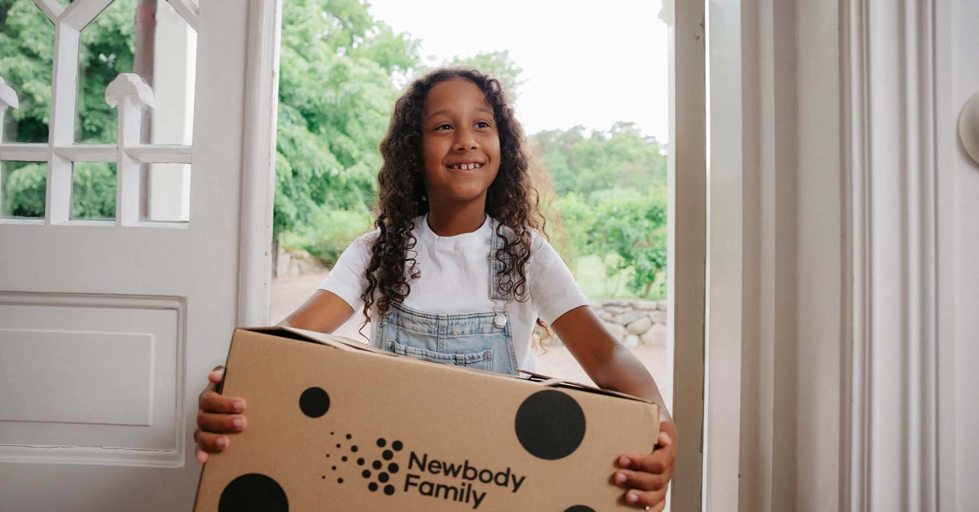 Glad tjej som står i en dörr öppning med en newbody katong i famnen