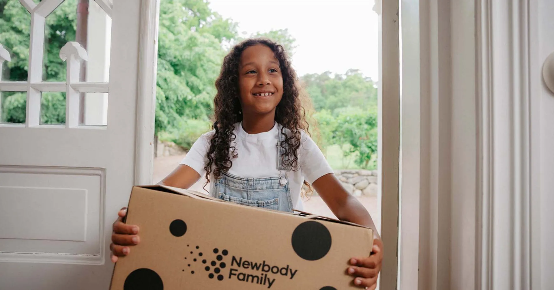 Glad tjej som står i en dörr öppning med en newbody katong i famnen