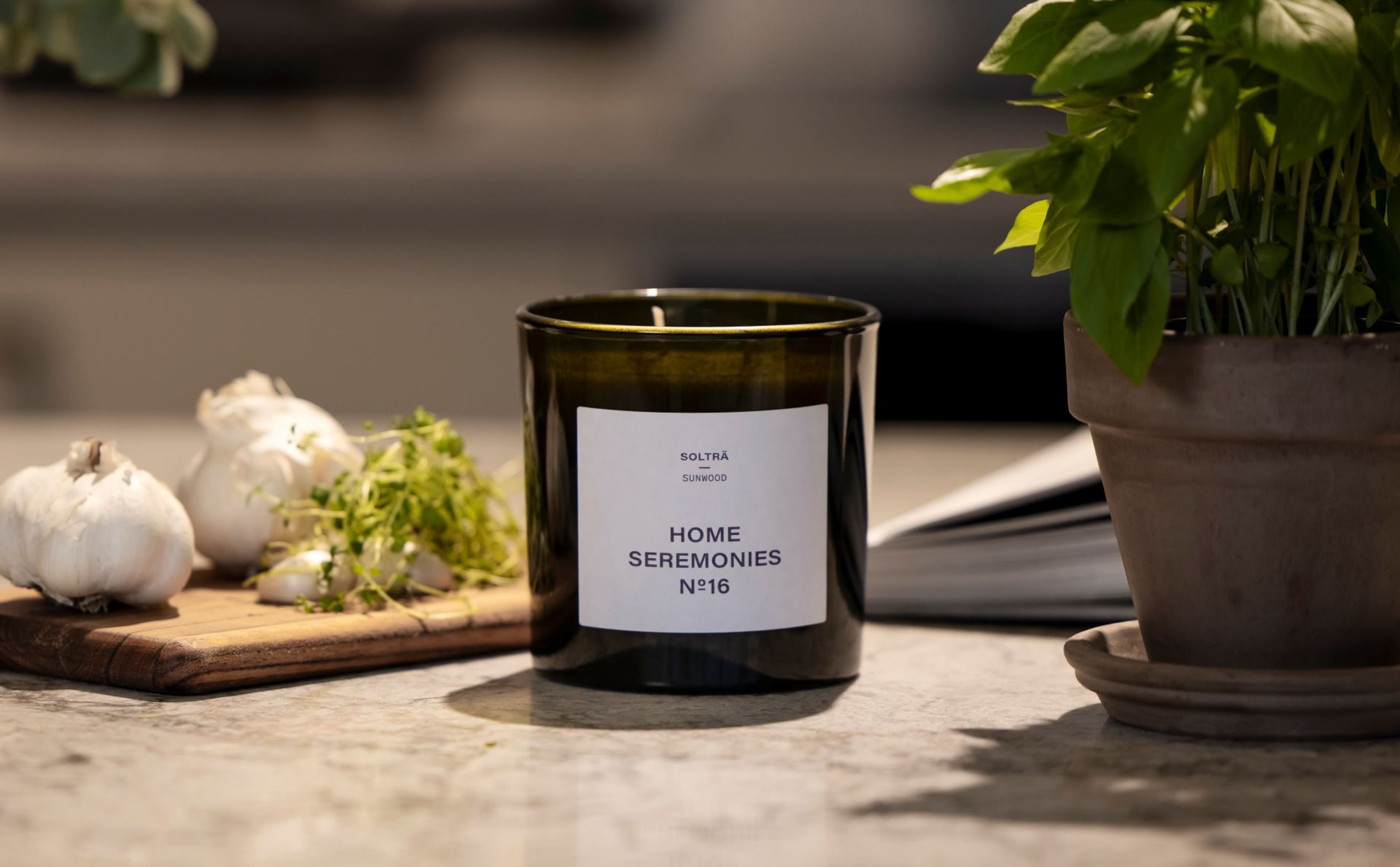 Doftljus står på en köksbänk med vitlök och basilika i bakgrunden