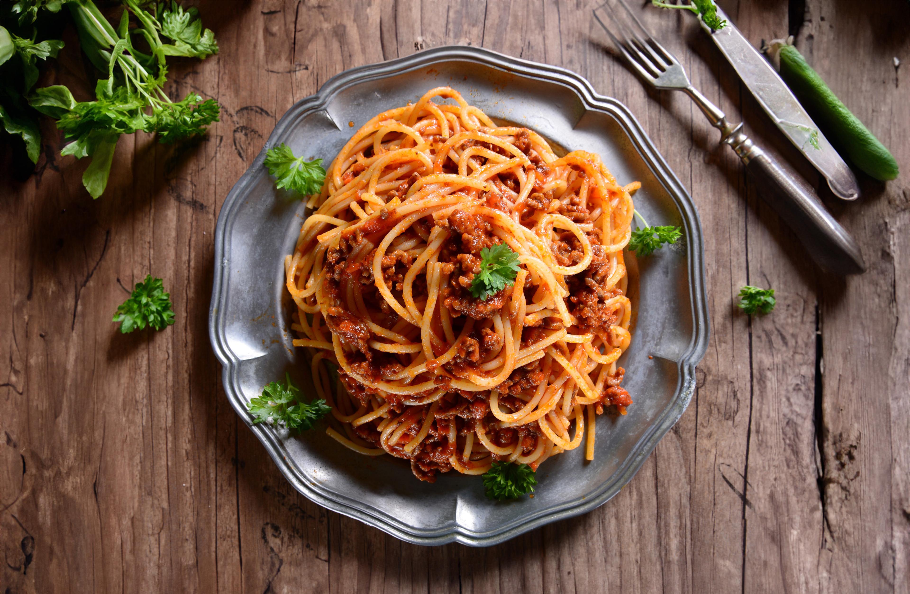 Tallrik med spaghetti och vegetarisk bolognese, garnerad med färsk persilja. Serverad på ett rustikt trädgårdsbord.