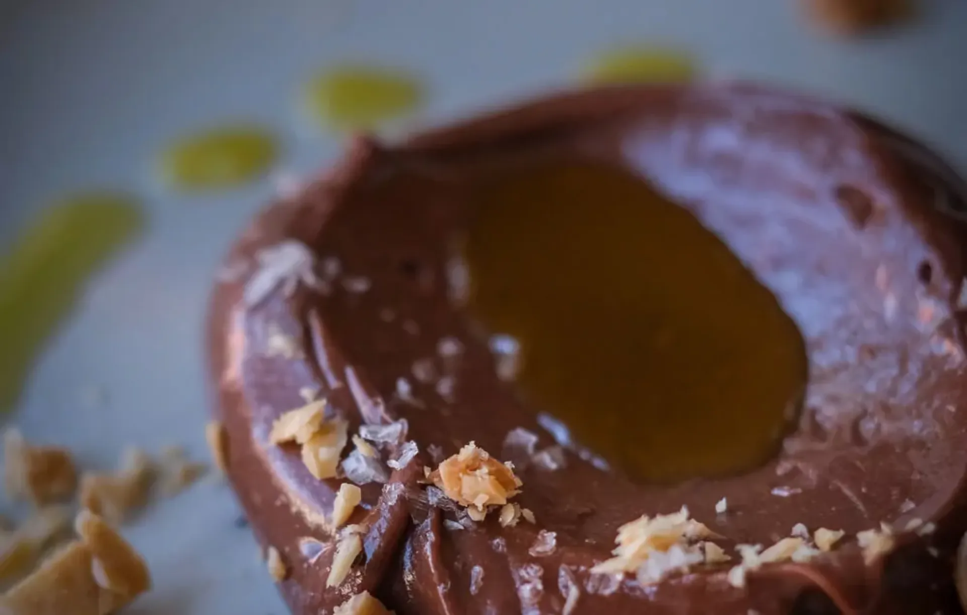 En rund chokladmousse med en klick gyllene sås i mitten och små smulor av nötter runt kanterna. Mjukt och krämigt med en fin glans på ytan.
