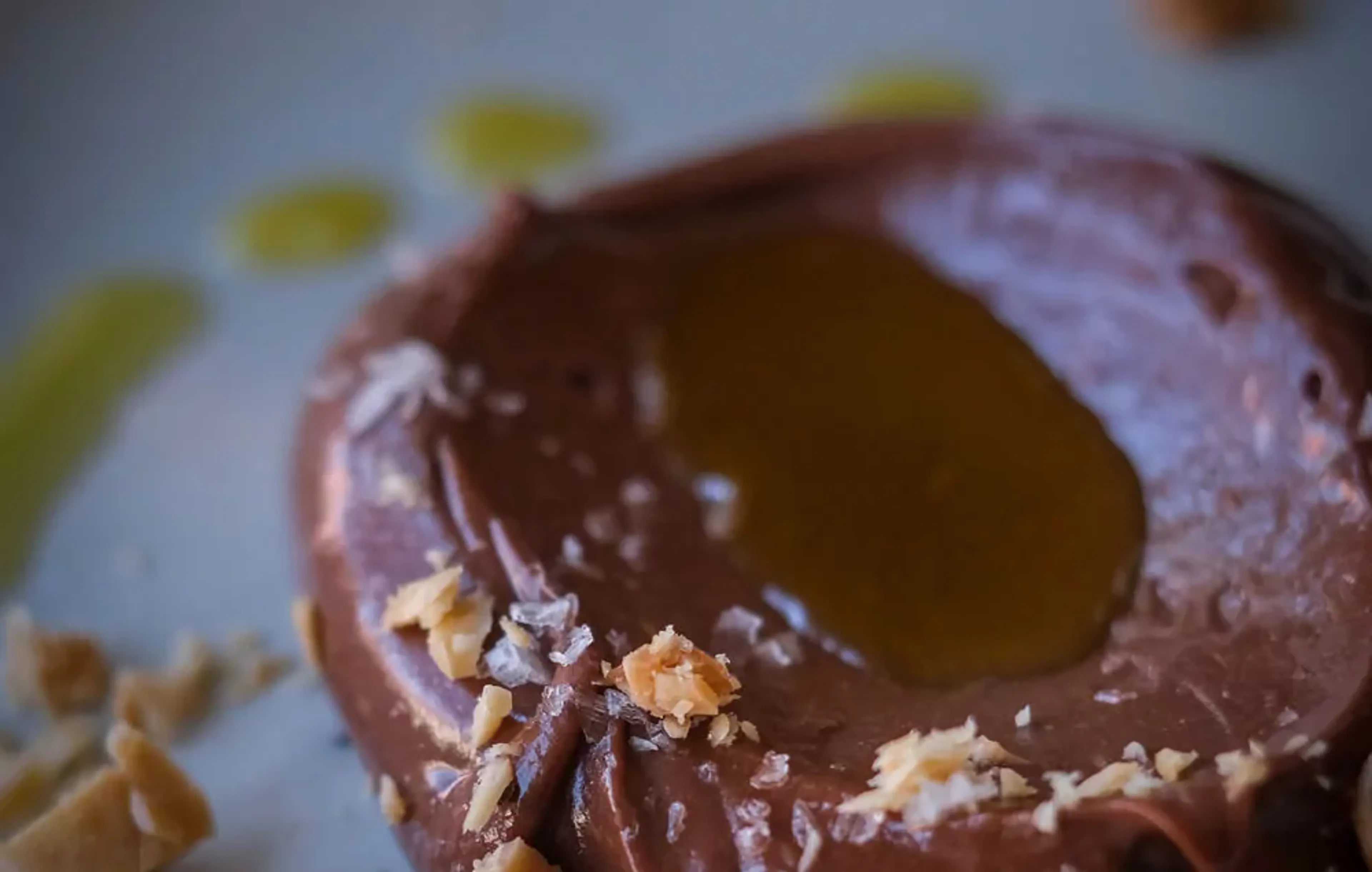 En rund chokladmousse med en klick gyllene sås i mitten och små smulor av nötter runt kanterna. Mjukt och krämigt med en fin glans på ytan.