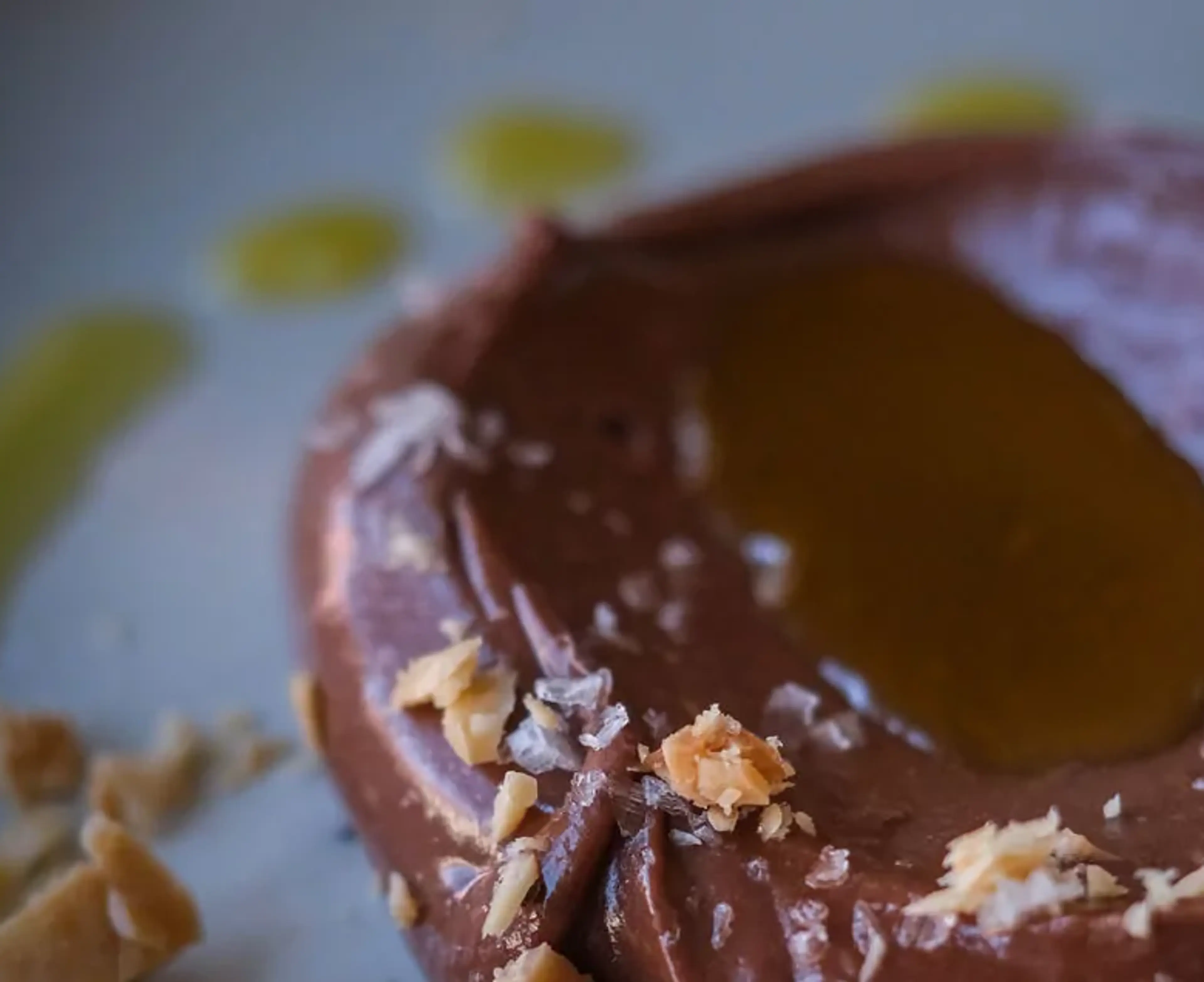 En rund chokladmousse med en klick gyllene sås i mitten och små smulor av nötter runt kanterna. Mjukt och krämigt med en fin glans på ytan.