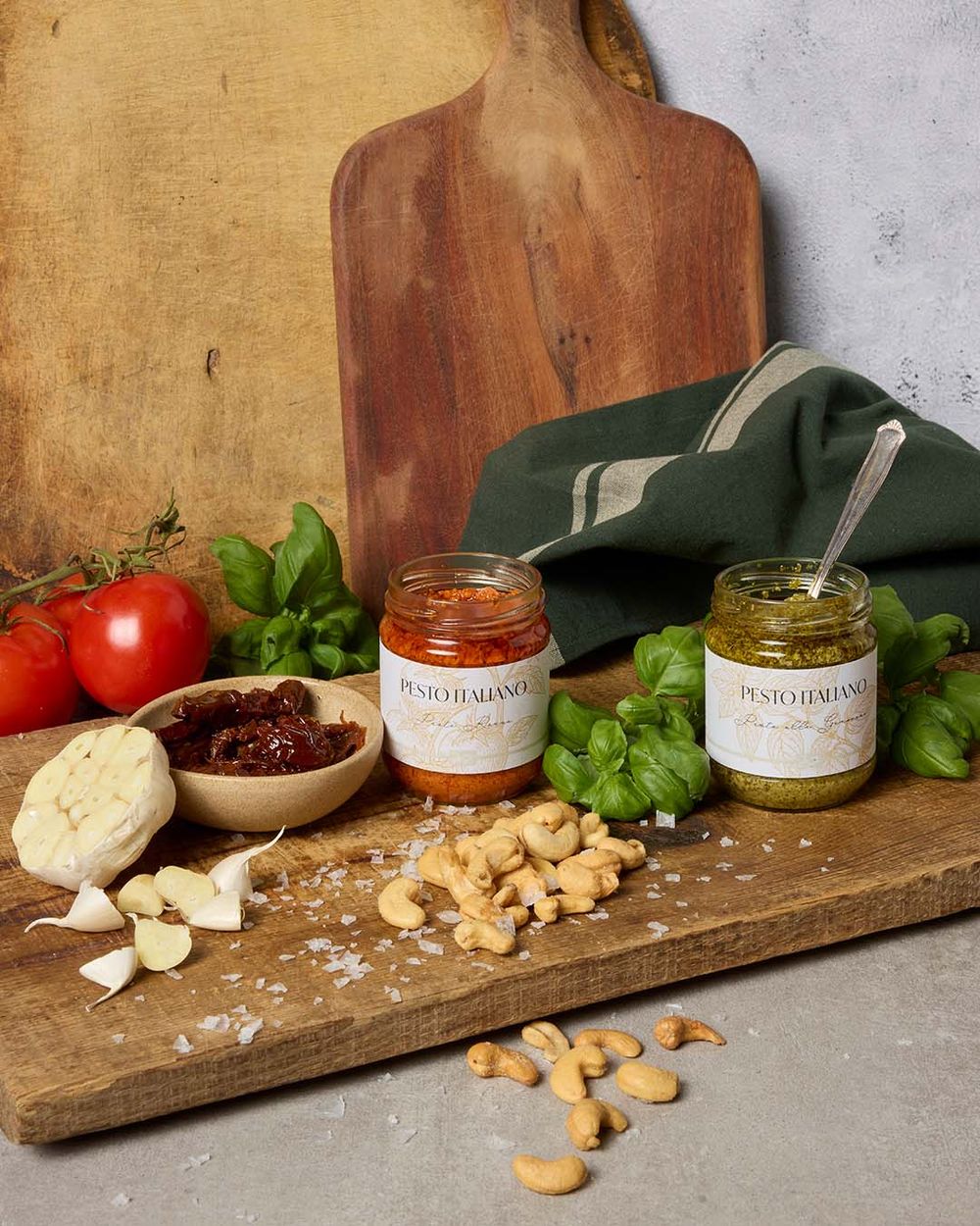 Röd och grön pesto i förpackning, stylad på köksbänk med ingredienser och tillbehör