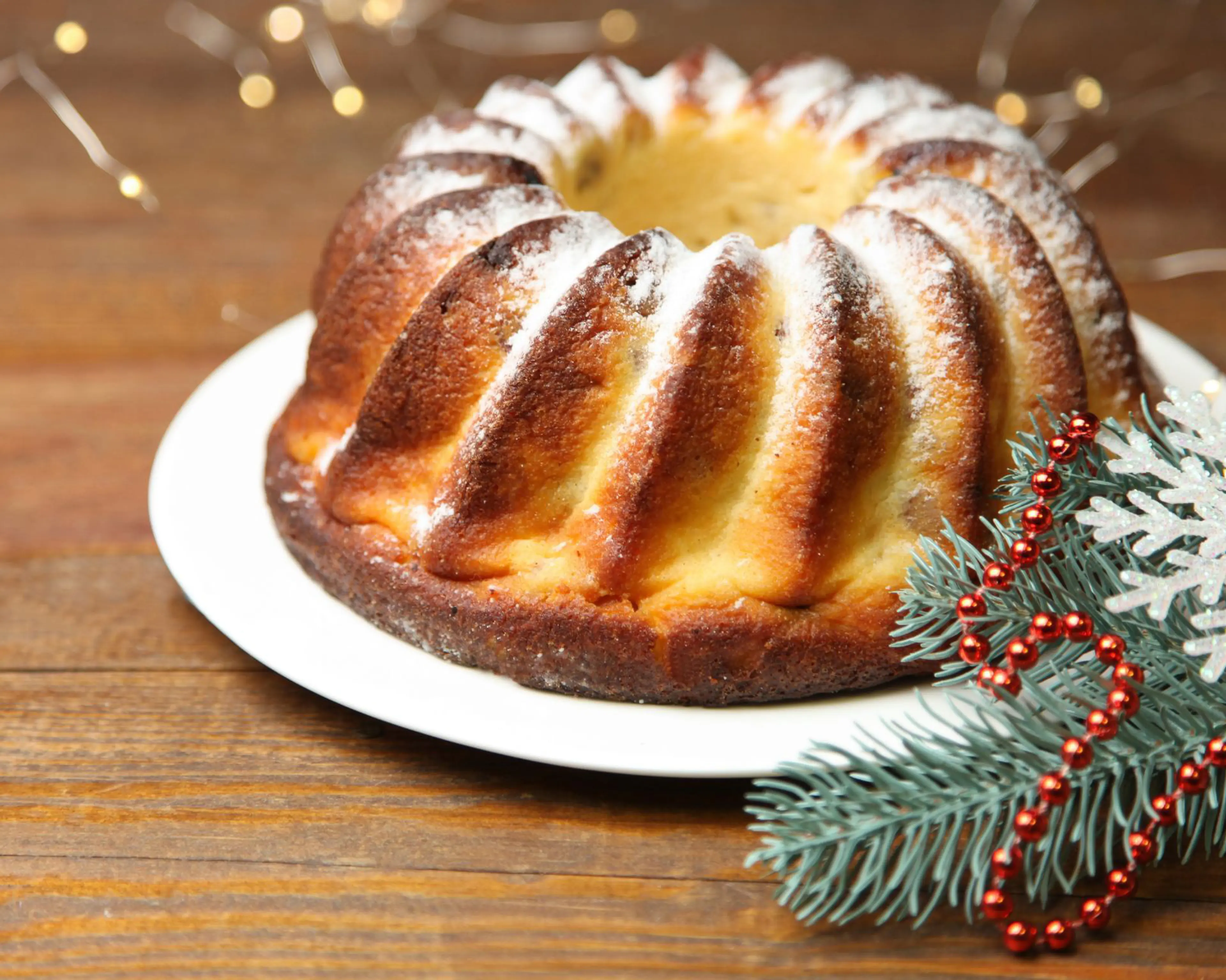 En saftig saffranskaka med en gyllene yta, pudrad med florsocker. Dekorerad med granris, röda kulor och en glittrande snöflinga för en julig känsla.
