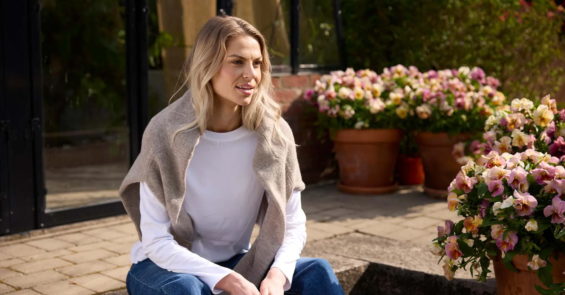 Vit långärmad bomullströja för dam, i bakgrunden är det rosa och gula blommor