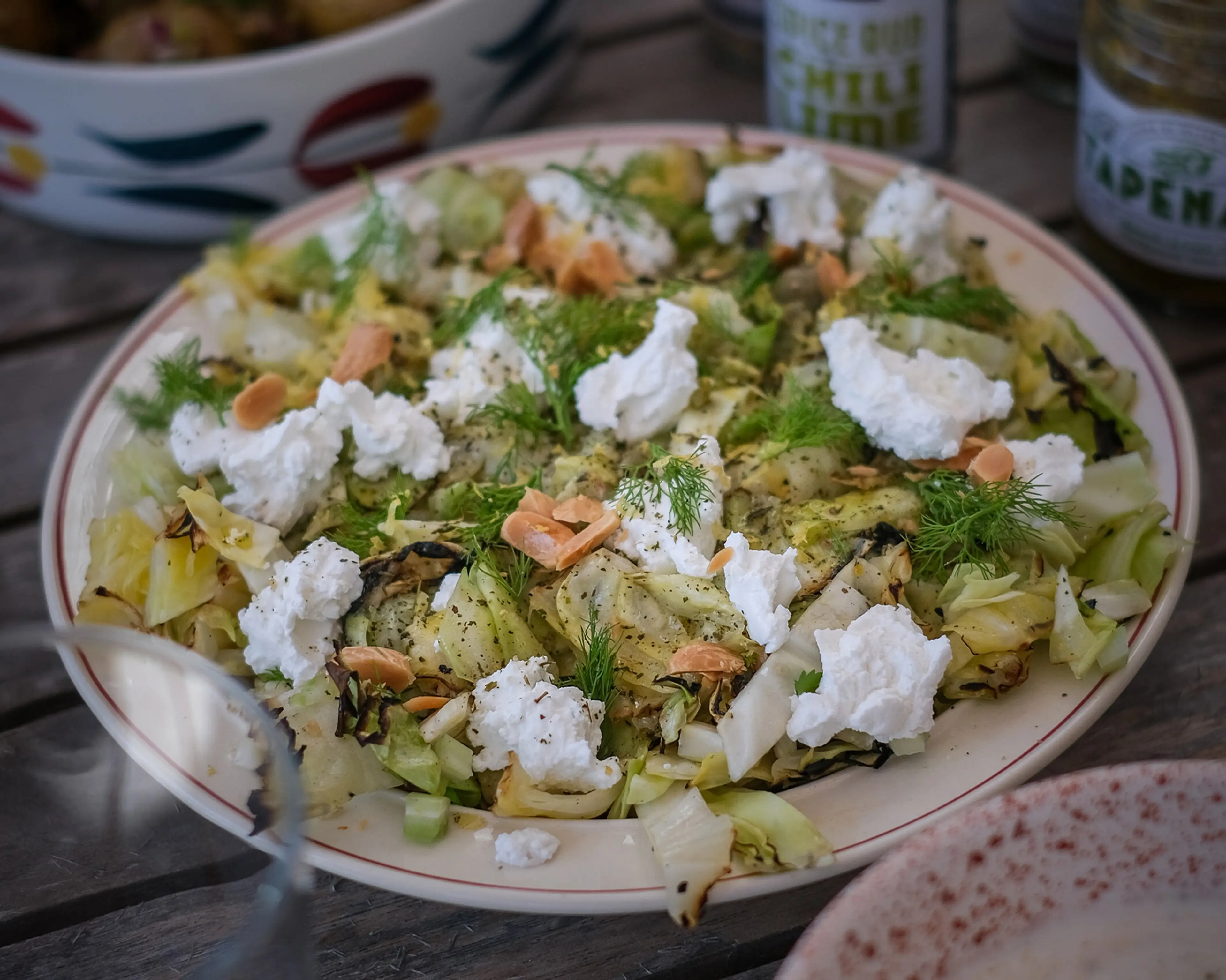 Grillad vitkål toppad med smulig ost, dill och rostad mandel på ett vitt fat. Färska örter och kryddor ger en fräsch och kryddig touch.