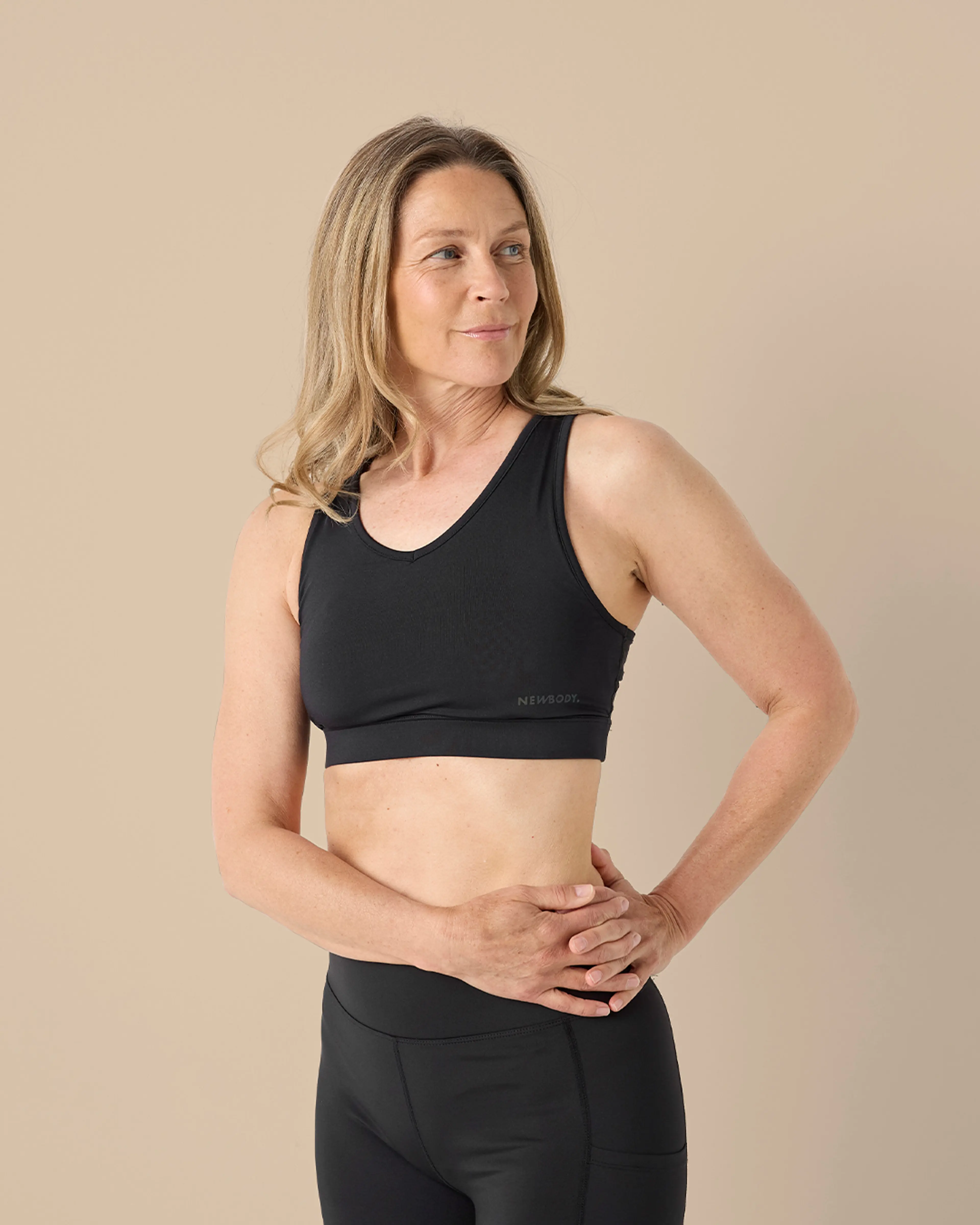 En svart sport-bh med breda axelband och diskret logga på sidan, designad för att ge stöd och komfort under träning. Modellen bär den tillsammans med svarta, högmidjade träningstights.