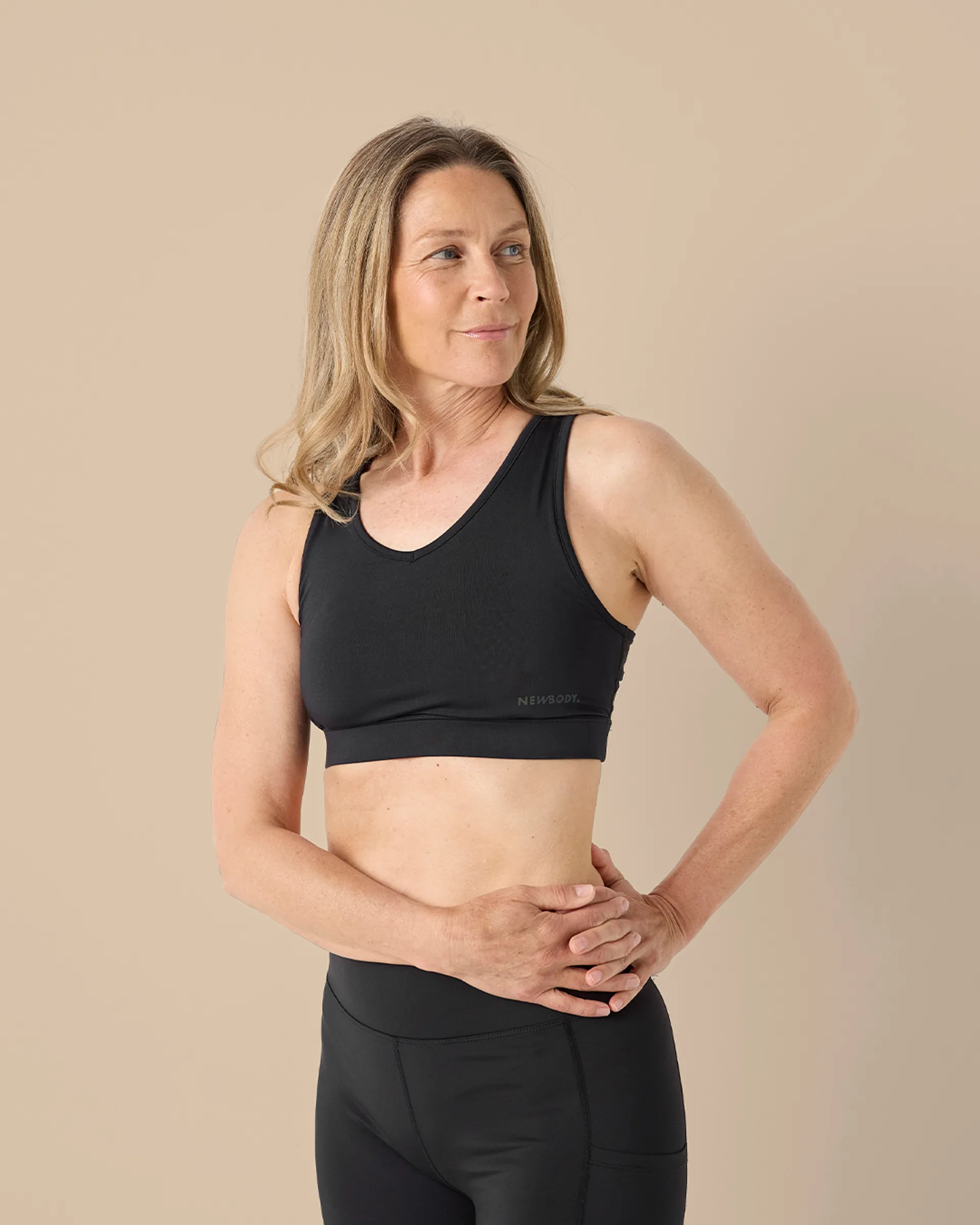 En svart sport-bh med breda axelband och diskret logga på sidan, designad för att ge stöd och komfort under träning. Modellen bär den tillsammans med svarta, högmidjade träningstights.