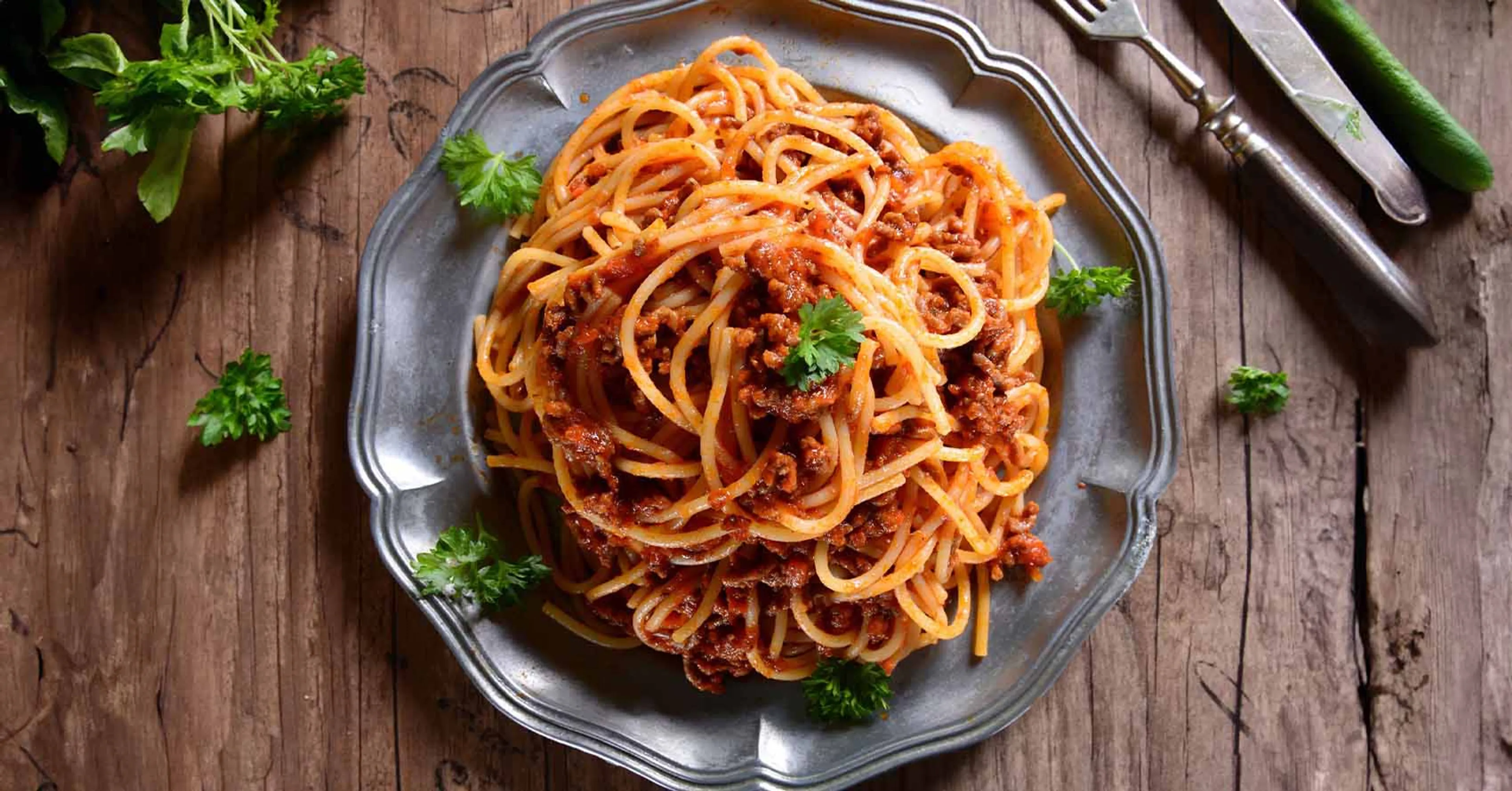 Tallrik med spaghetti och vegetarisk bolognese, garnerad med färsk persilja. Serverad på ett rustikt trädgårdsbord.