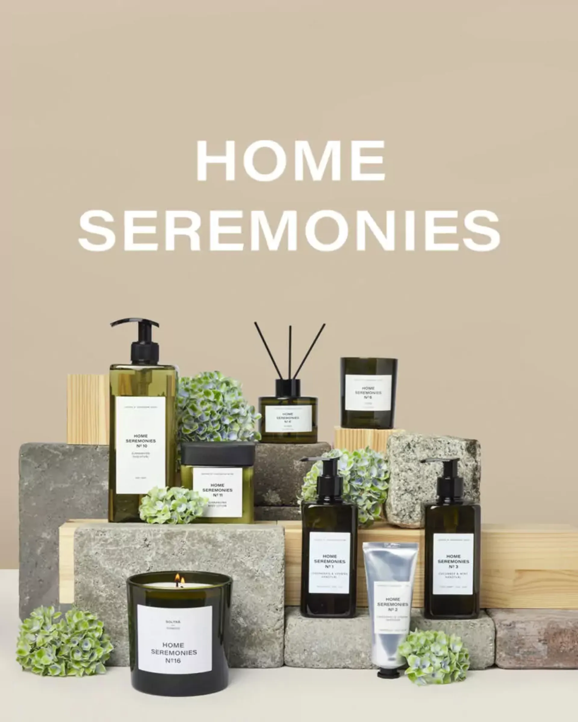 Ett urval av doftljus, handkräm, tvålpump och doftpinnar i stilrena, gröna och svarta förpackningar, arrangerade med stenblock och dekorativa blad. Texten "HOME SEREMONIES" syns tydligt ovanför produkterna
