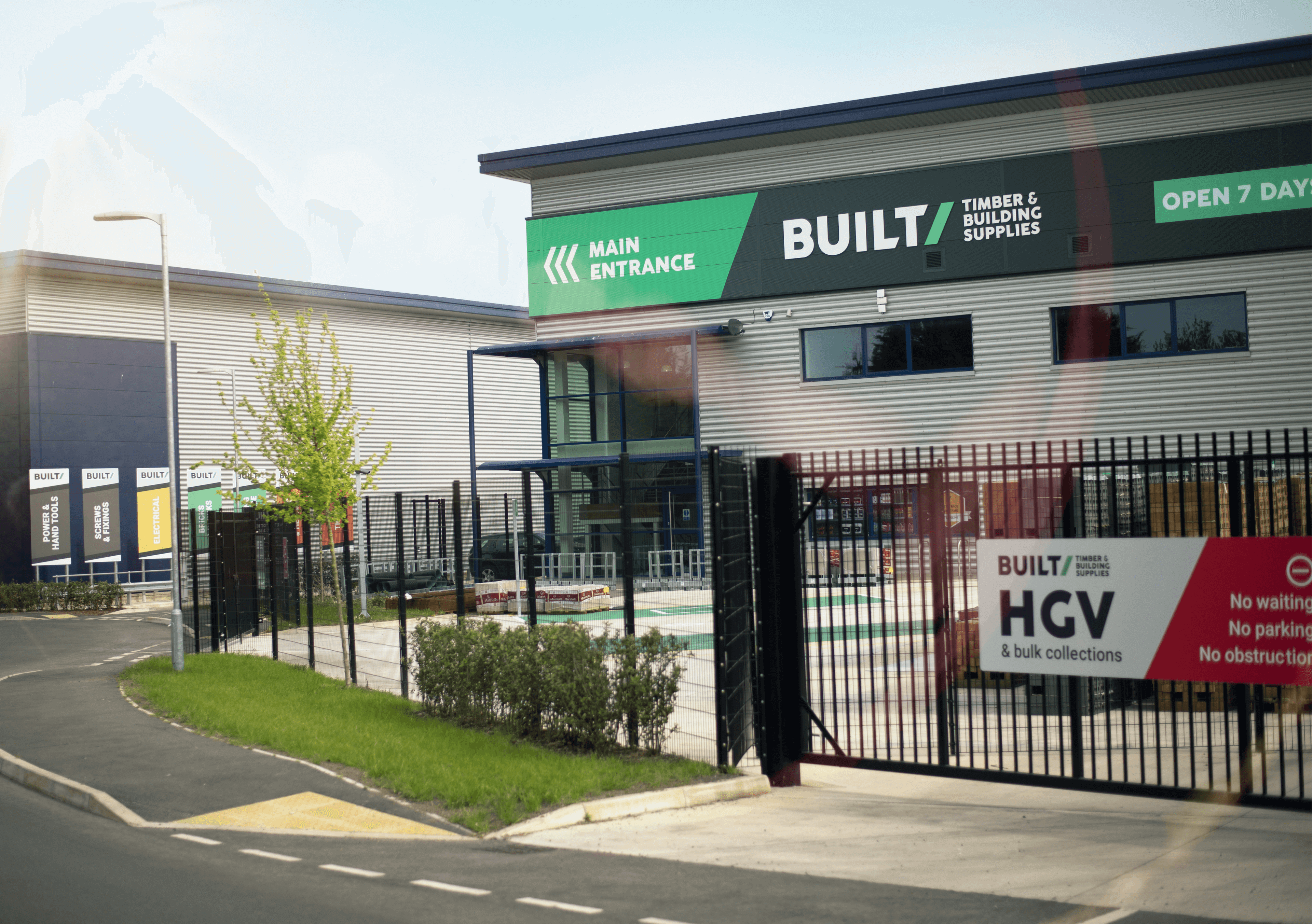 A grey warehouse with Built singage along the top. The warehouse sits behind black gates with a Built sign on them.