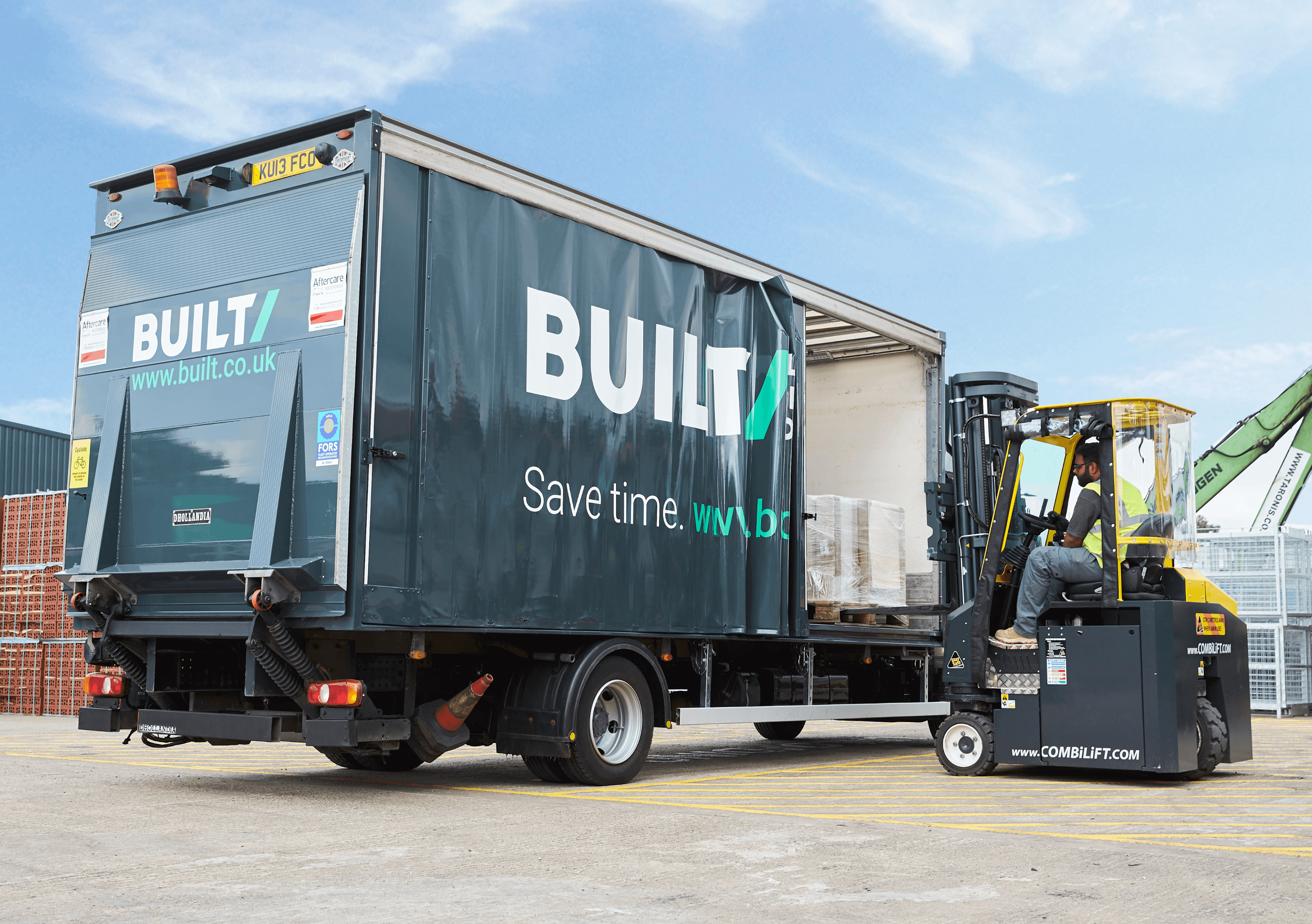 Built builders merchant branded delivery truck getting loaded by a forklift in an outdoor warehouse