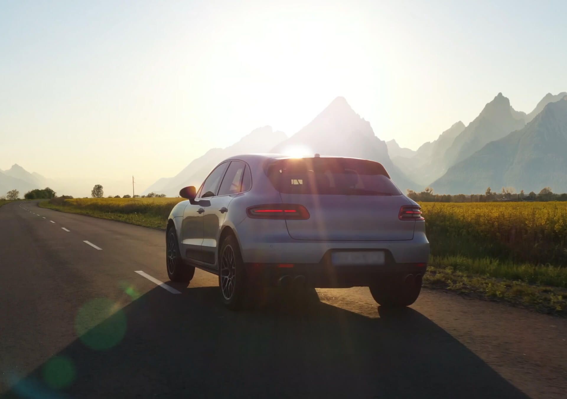 A silver car driving along a scenic road with sharp mountain peaks in the background