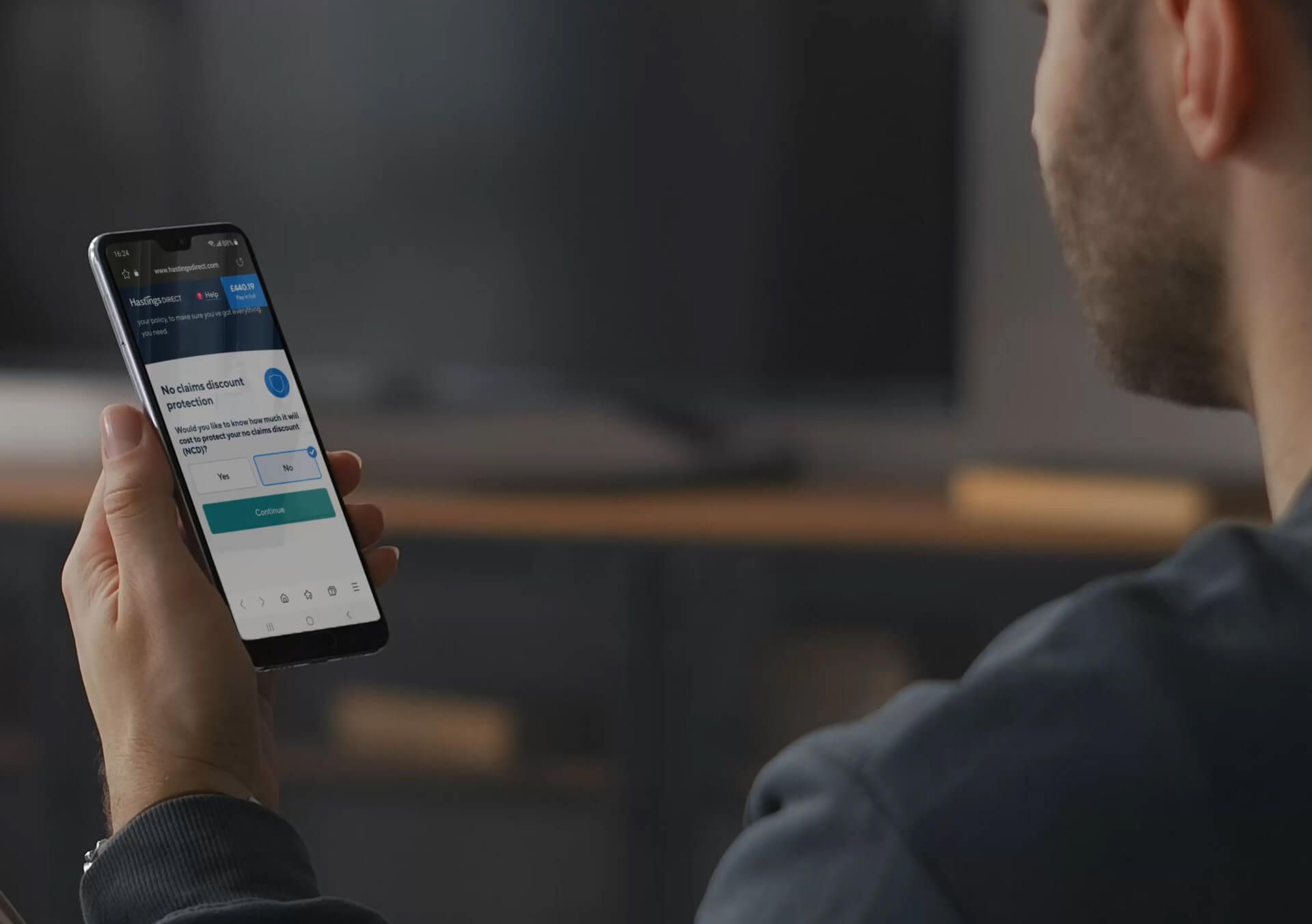 A photo of a man holding a phone with the No claims discount screen on.