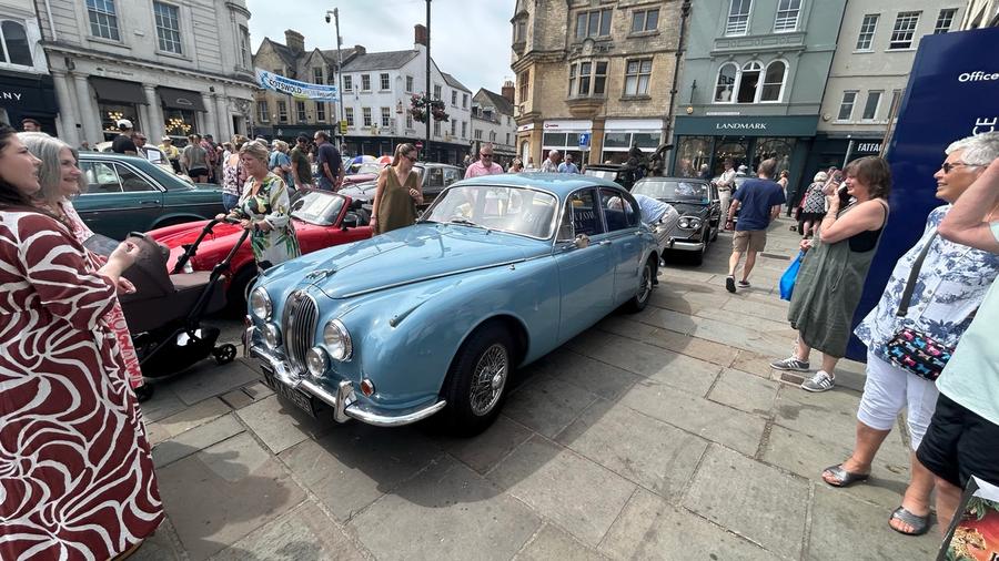 A powder blue Jaguar Mk2 saloon with chrome wire wheels, parked among the crowd on the Market Place flagstones.