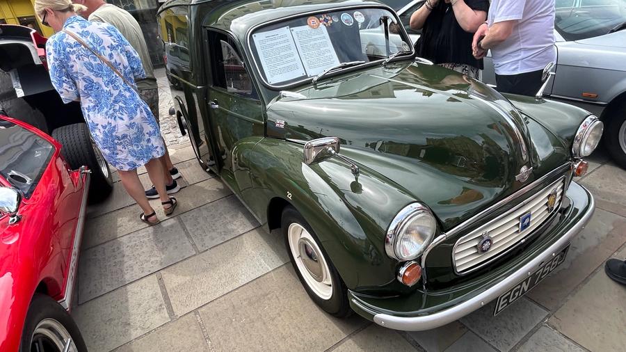 A dark green Morris Minor van in immaculate condition, with an information sheet displayed in its windscreen, parked near Santander on the Market Place.
