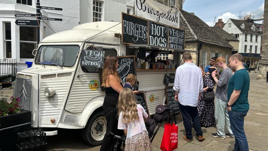 A white Citroen H van trading as Burgerlish, with chalkboard menus for burgers, hot dogs and vegan options, and families queuing alongside.