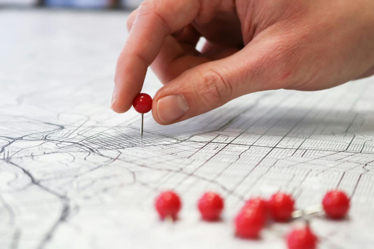 Hand setzt rote Stecknadeln auf einen Stadtplan zur Planung von Drehorten