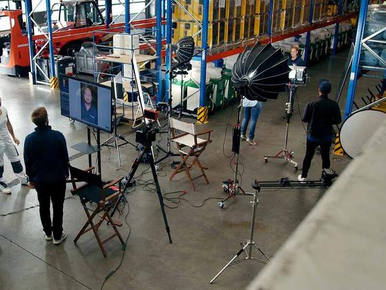 Filmteam mit Kamera, Licht und Kontrollmonitor in einer Lagerhalle