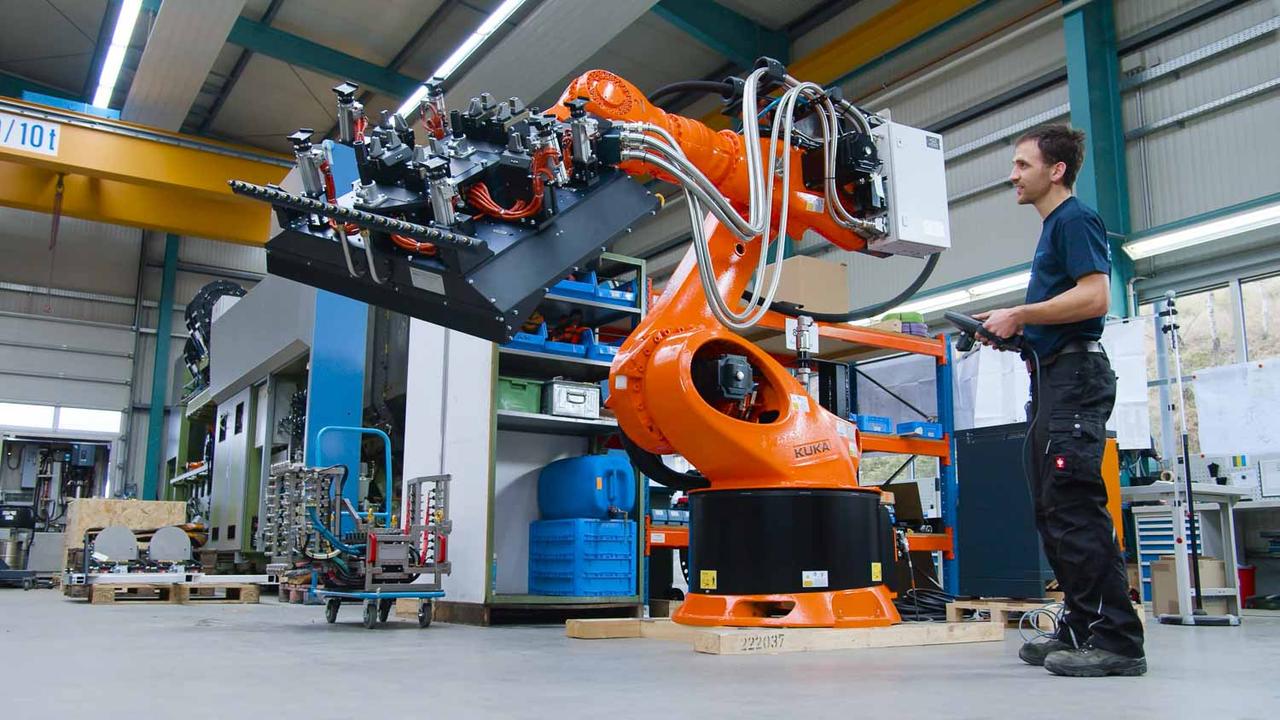 Still aus dem Böhmer-Imagefilm: Mitarbeiter steuert einen orangefarbenen KUKA-Roboterarm in der Halle