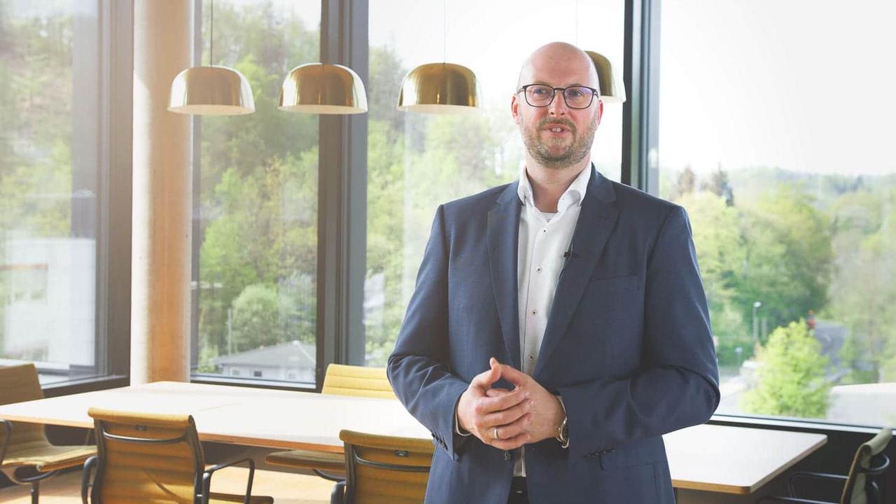 Manager im Anzug spricht in einem hellen Konferenzraum in die Kamera – Quartalsrückblick in Videoform