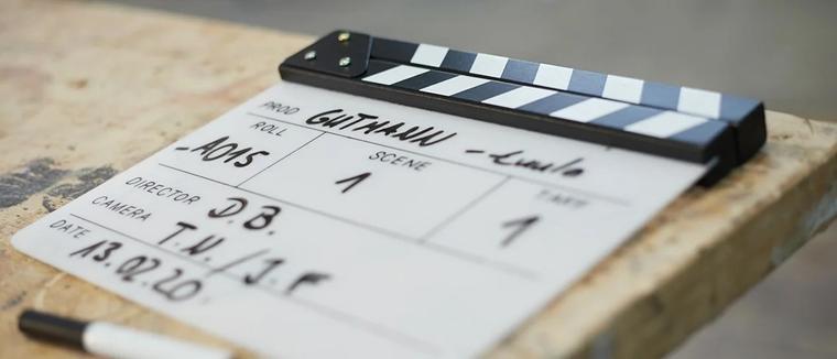 Filmklappe mit handschriftlichen Produktionsangaben liegt auf einem Holztisch am Filmset