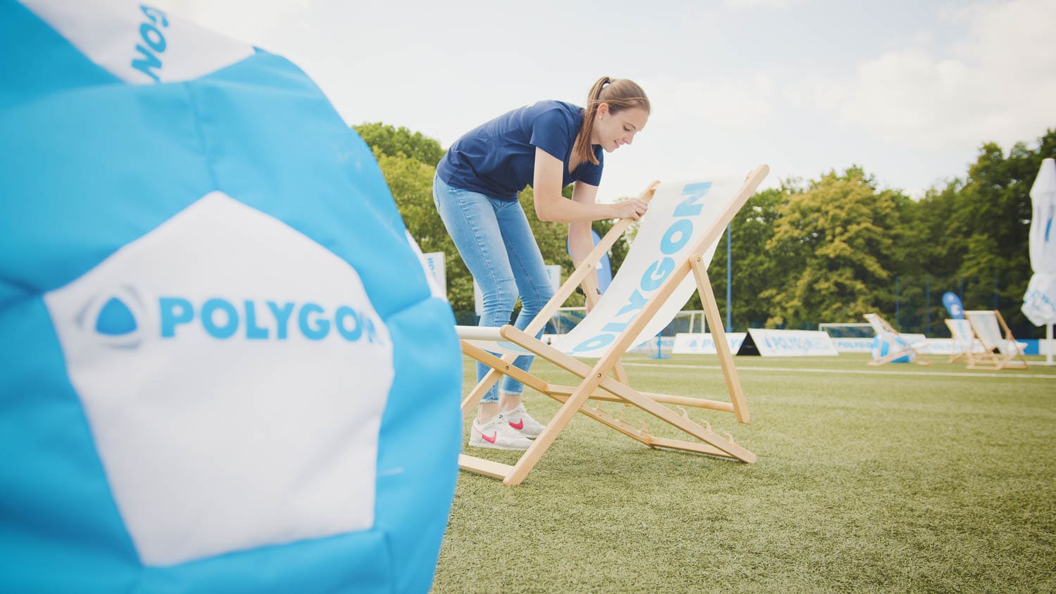 Eine Person stellt eine hölzerne Staffelei mit dem „Polygon“-Logo für eine Videomarketing-Präsentation bei einer Veranstaltung im Freien auf.