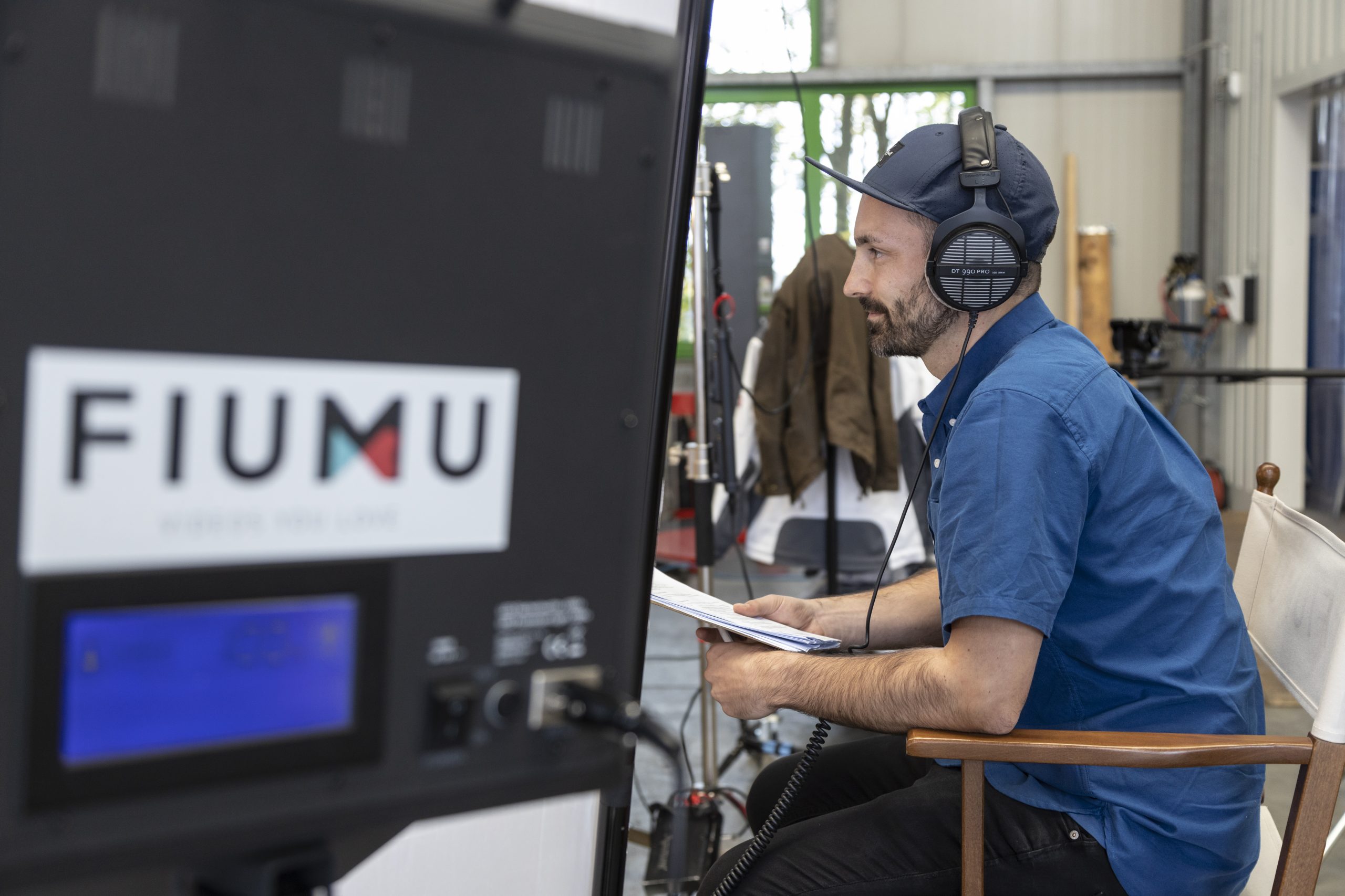 FIUMU-Regisseur mit Kopfhörern und Drehbuch am Set-Monitor mit FIUMU-Logo während eines Imagefilm-Drehs