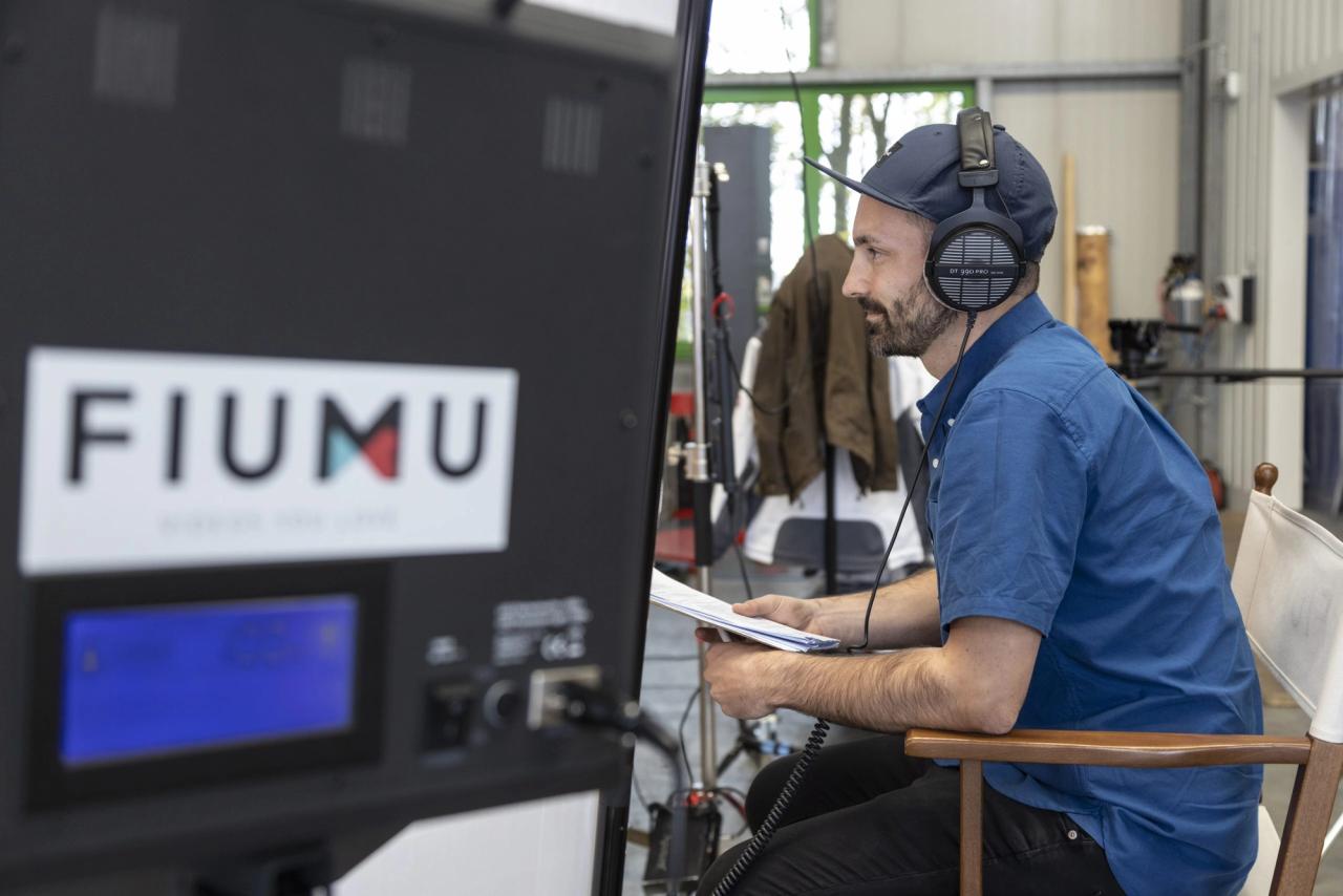 FIUMU-Regisseur mit Kopfhörern und Drehbuch am Set-Monitor mit FIUMU-Logo während eines Imagefilm-Drehs