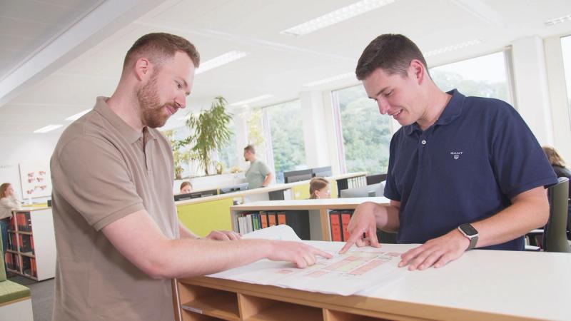 G-TEC: zwei Kollegen besprechen einen Plan im Großraumbüro