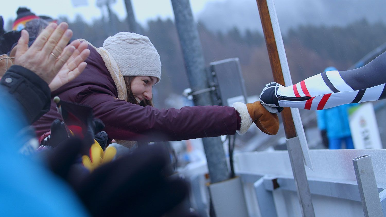 Zuschauerin klatscht einen Rennrodler bei einem Wintersport-Event im Schnee ab im Eventfilm