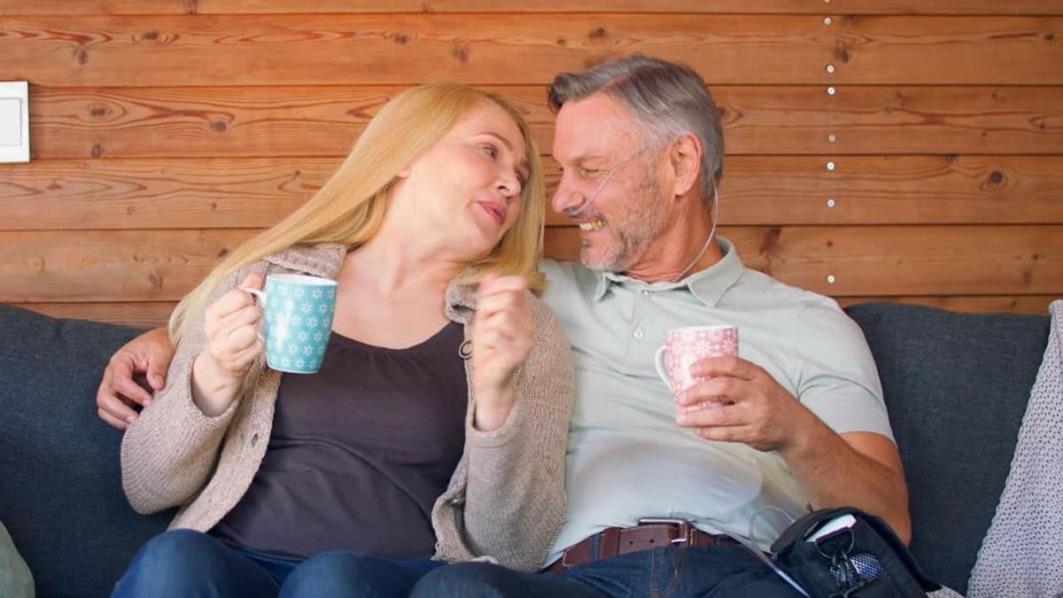 Ein Paar sitzt mit Kaffeetassen auf einem Sofa vor einer Holzwand