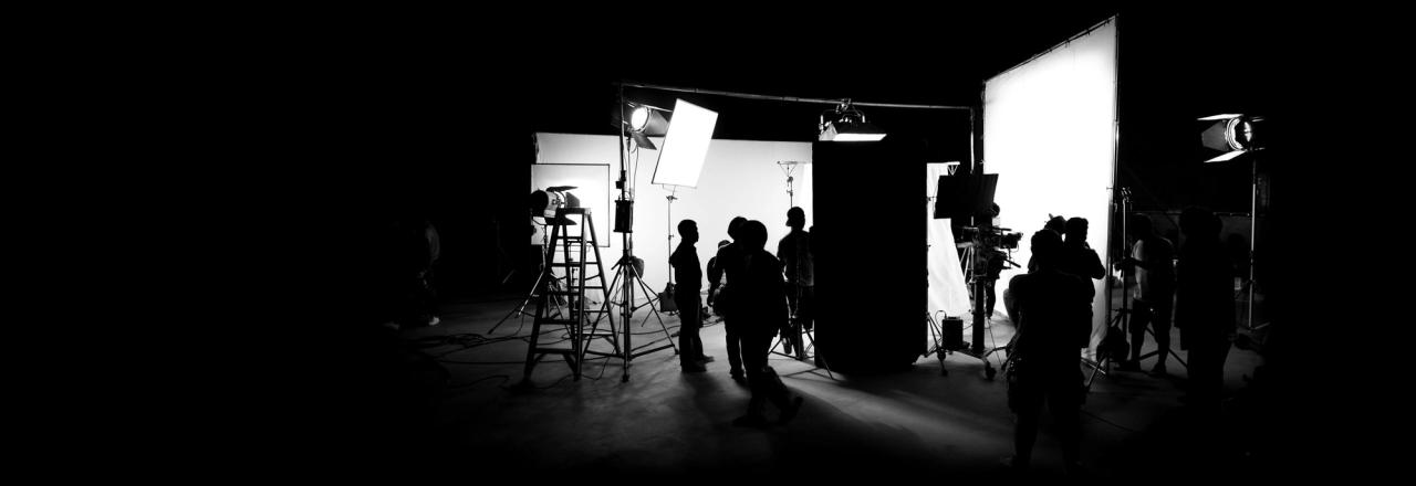 Eingerichtetes Filmset an einem Drehtag: Crew, Scheinwerfer und Kamera im abgedunkelten Studio
