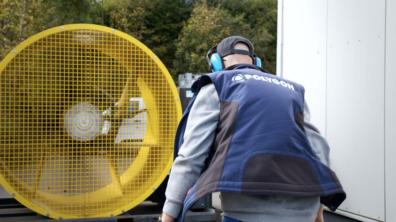 Mitarbeiter mit Gehörschutz neben dem gelben Axialventilator von POLYGON