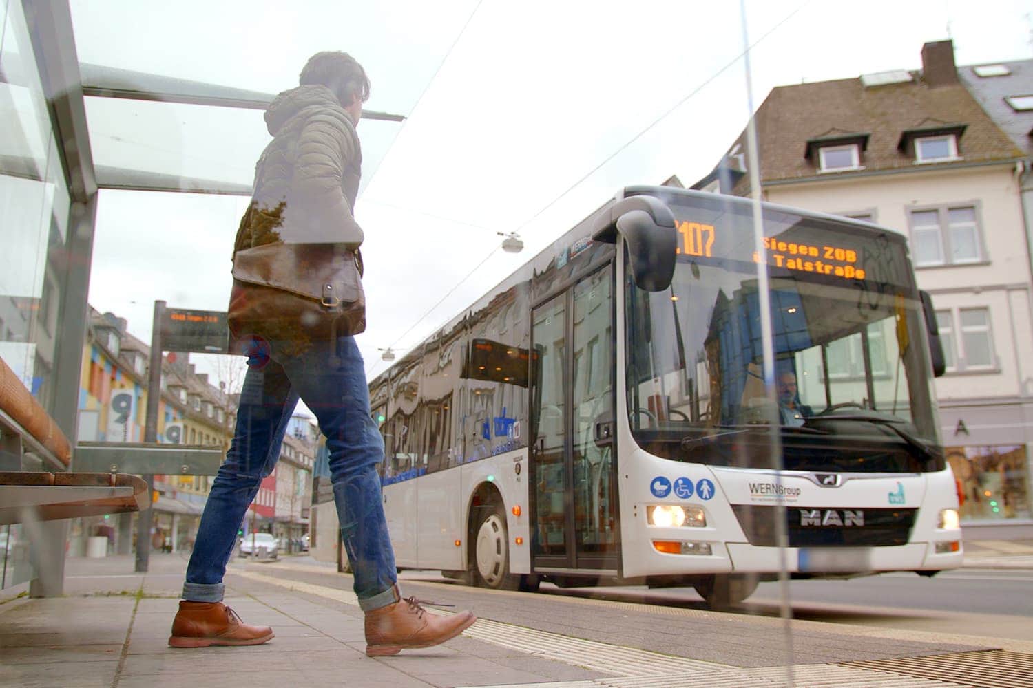 Fußgänger an einer Bushaltestelle in Siegen, im Hintergrund fährt ein weißer Linienbus ein