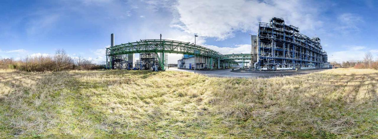 360-Grad-Panorama einer Industrieanlage mit Rohrbrücken unter blauem Himmel und Wiese im Vordergrund