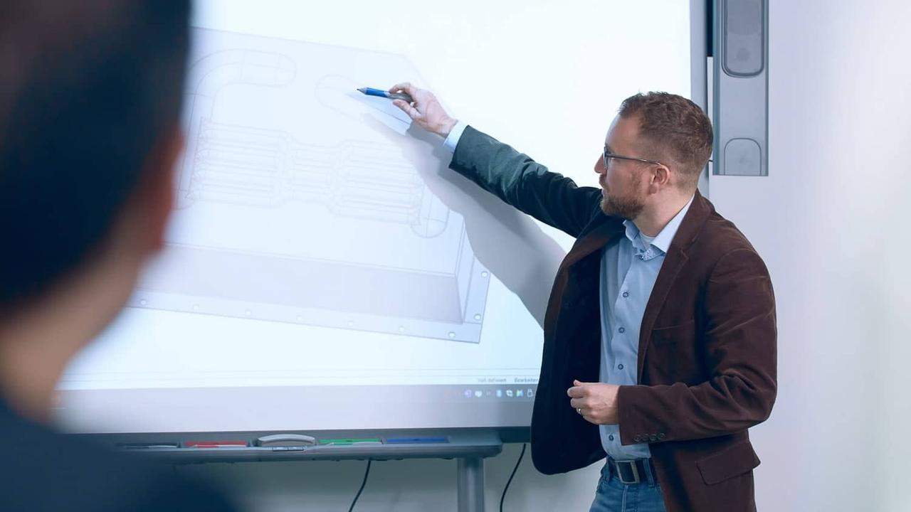 Referent erläutert an einem Whiteboard eine technische Zeichnung – Video-Keynote der Geschäftsleitung