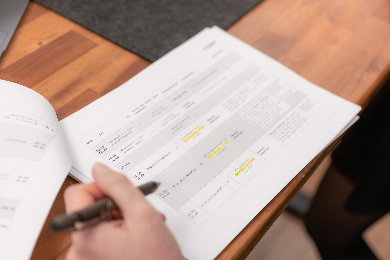 Hand mit Stift über einem ausgedruckten Drehplan mit Szenen-, Orts- und Zeitangaben